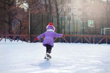 Kışın buz pateni pistinde bir kız paten kayar. Şehirdeki avluda buz pateni pistinde. Çocuk paten yapmayı öğreniyor.