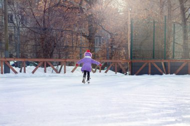 Kışın buz pateni pistinde bir kız paten kayar. Şehirdeki avluda buz pateni pistinde. Çocuk paten yapmayı öğreniyor.