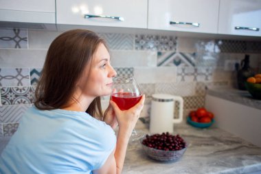 Bir kadın evdeki mutfağında yalnız başına şarap içer ya da içer. Tek başına alkol içmek. Bir bardak şarap.