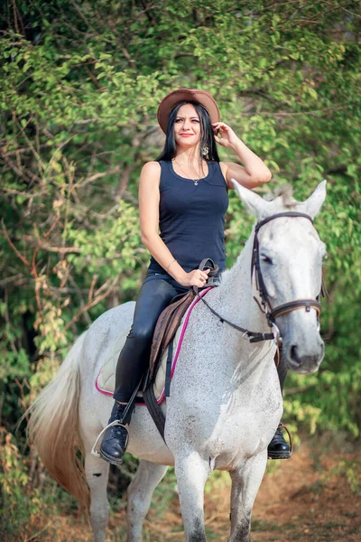 一个戴着牛仔帽 穿着皮裤的漂亮女人骑着一匹灰马 骑马训练 — 图库照片