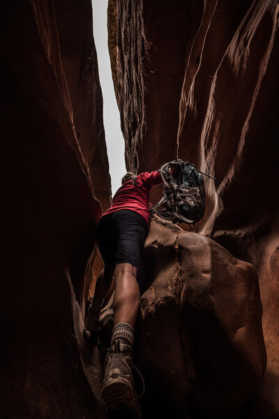 Woman with backpack climbing over large boulder inside Little Wi