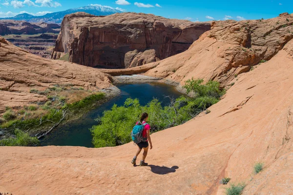 Hiker walking down the slick rock towards small lake — Stock Photo, Image