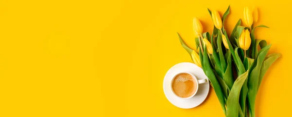 Coffee mug with bouquet of yellow tulips and copy space for notes good morning on bright yellow table, beautiful breakfast, vintage card, top view, flat lay, 8 march, woman day, mother day, romance