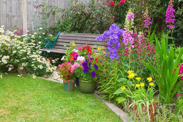 Jardim de casa de campo com banco e recipientes cheios de flores — Fotografia de Stock