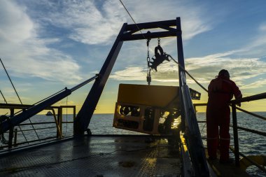 Güney Çin Denizi 'nin ortasında petrol ve doğalgaz boru hattı denetimi sırasında deniz yüzeyine girdikten sonra robotik uzaktan kumandalı aracı (ROV) ele geçiren işçilerin silueti