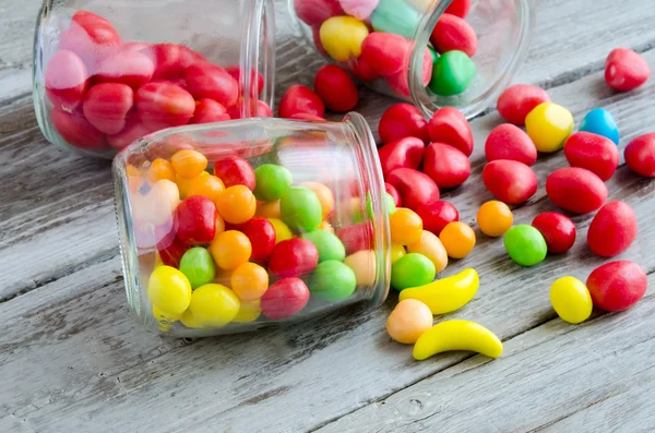 Bonbons in der Nähe von Glas mit bunten Süßigkeiten verstreut — Stockfoto