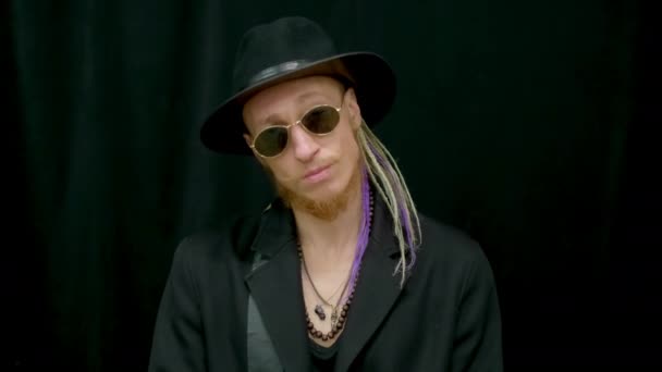 Portrait hipster dreadlocks looking at camera in hat. Rocker man in sunglasses. — Stock Video