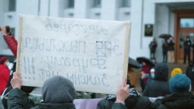 Ralli eylemcileri pankartlarla ayakta dururlar. Protestocular siyasi afişleri ellerinde tutuyorlar.