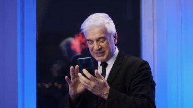 Beyaz tenli, yaşlı bir beyefendi havai fişekler sırasında akıllı telefondan mesaj atıyor..