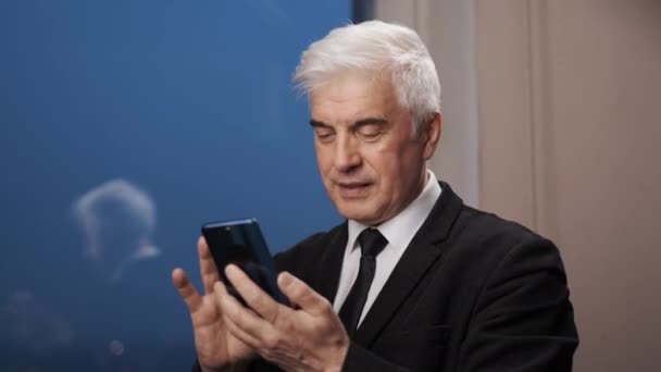 Pensive gentleman v obleku hledá přes smartphone. Starší šedý muž přemýšlí — Stock video