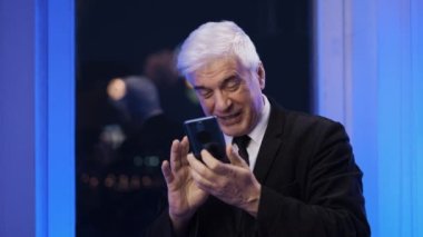 Havai fişeklerin altında cep telefonlu, spor ceketli, yaşlı ve neşeli bir adam.