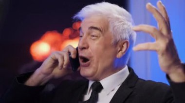 Blazer ceketli, kıkırdayan ve gülümseyen yaşlı iş adamı havai fişekler atarken telefonla konuşuyor.