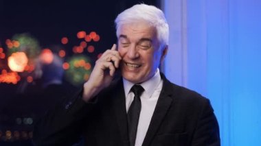 Takım elbiseli gülen yaşlı işadamı akıllı telefondan konuşuyor. Havai fişek patlamaları