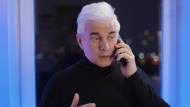 Balıkçı yaka kazak giyen olgun beyefendi telefonla konuşuyor. Gri saçlı adam.