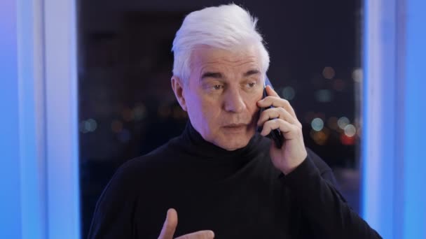 터틀넥 점퍼에서 핸드폰으로 강연하는 성인 신사. 흰머리 사람 — 비디오