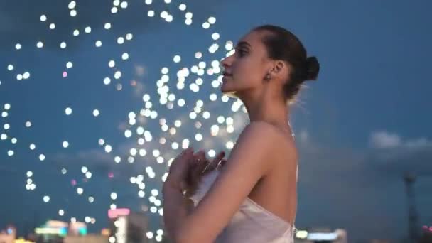 นักบัลเล่ต์เต้นบัลเล่ต์ที่น่าตื่นตาตื่นใจที่พื้นหลังเรืองแสงดอกไม้ไฟบนหลังคาคืนเมือง . — วีดีโอสต็อก