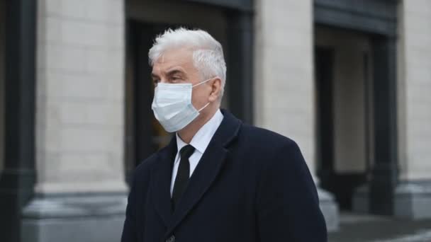 Hombre de pelo gris y mascarilla debido a los paseos pandémicos por las calles vacías de la ciudad. — Vídeos de Stock