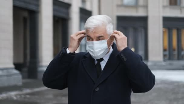 Eldre mennesker tar på seg maske 19. Gammel, grå forretningsmann med ansiktsmaske. – stockvideo