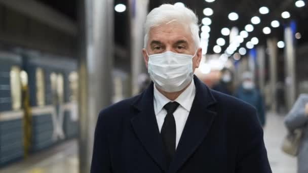 Elegante hombre de negocios con abrigo negro y mascarilla camina en la estación de metro. — Vídeos de Stock
