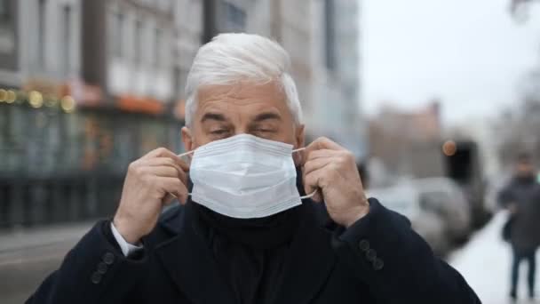 Vieux monsieur aux cheveux gris dans les rues d'Amsterdam met sur le masque du coronavirus. — Video