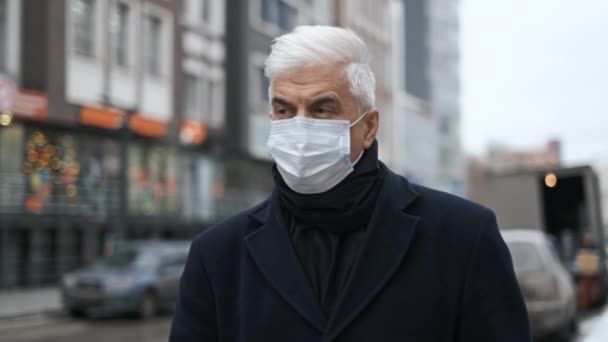 Cavalheiro mascarado com cabelos grisalhos em casaco preto e camisa caminha nas ruas da cidade — Vídeo de Stock