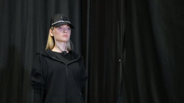 Chica en gorra de diseñador con cadenas camina en el podio pasarela. Desfile de moda. — Vídeos de Stock