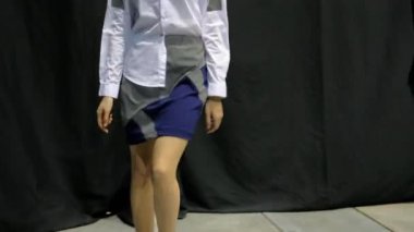 Podyum podyumunda yürüyen iki kız. Üzerlerinde mavi etek ve pembe pantolon var..