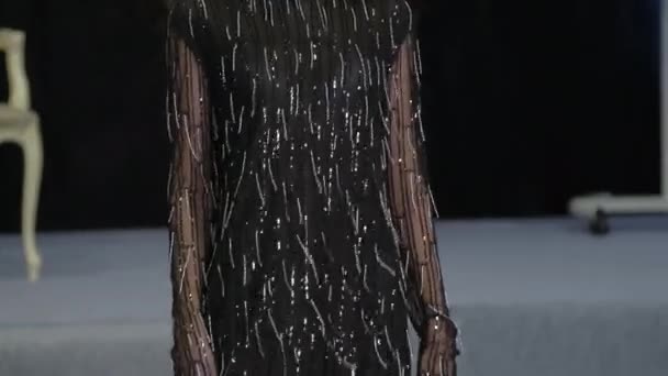 Brunette vrouwelijke model lopen op het podium. Meisje in zwarte jurk met franje patroon. — Stockvideo