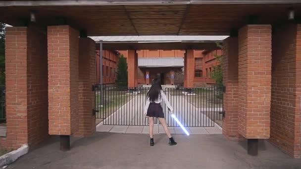 Девушка-воин в юбке Скотта стоит со световым мечом перед постройкой — стоковое видео