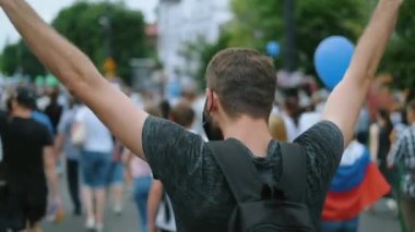 Elleri havada maskeli bir adam siyasi eylem mitinginde bayrak tutuyor.