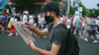 Maskeli çevik kuvvet eylemcisi afiş çiziyor, afiş asıyor. Asiler toplanıyor..