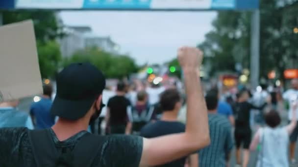 Agitant le bras et le poing, un militant manifestant marche dans une foule émeute avec une bannière à la main. — Video