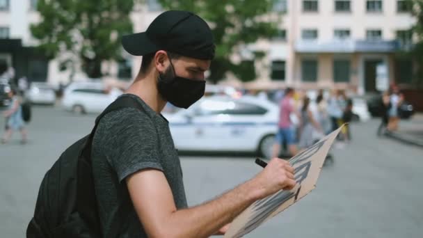 Manifestante masculino dibujando pancarta en las manos con letrero en la multitud de manifestantes. — Vídeos de Stock