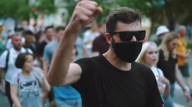 Siyah gözlüklü ve maskeli protestocu kalabalığın üzerinde el sallıyor..