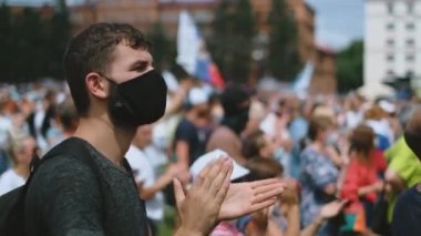 Siyasi miting kalabalığında maskeli protestocuları alkışlamak.