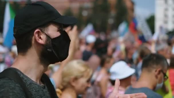 Oklaski męski aktywista w masce i czapce stoi wśród opozycji ludzie bunt. — Wideo stockowe