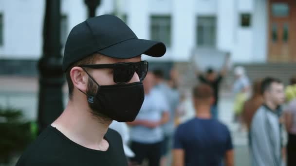 Агент секретной службы в черных очках, кепке и маске на митинге протестующих. — стоковое видео