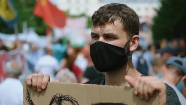 Zamaskowany protestujący aktywista z tabliczką na transparencie stoi przeciwko restrykcjom. — Wideo stockowe