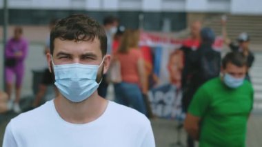 Coronavirus maskeli miting eylemcisinin portresi şehirde protesto kalabalığı arasında.