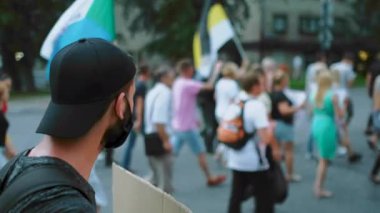 Koronavirüslü erkek protestocu, Rus bayraklarıyla barışçıl kalabalıkta maske takıyor..