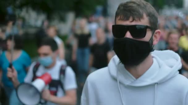 Biljett upplopp man i ansiktet mask med megafon i bakgrunden på trångt protest. — Stockvideo