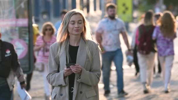 Femme d'affaires blonde marchant dans les rues du centre-ville tout en envoyant des SMS sur smartphone. — Video