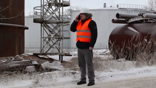 Ingenieur praten op de smartphone in de buurt van de olietanks — Stockvideo