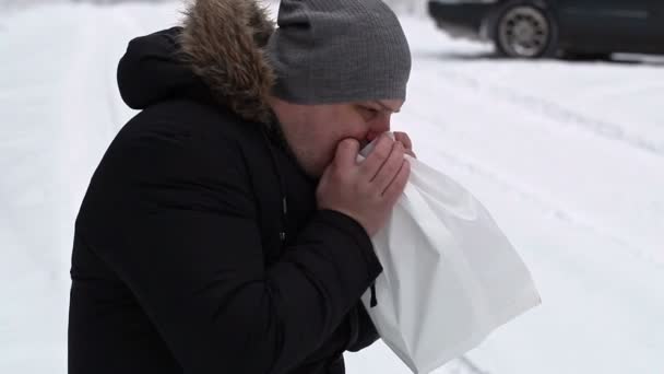 Стресовий чоловік вдихає паперовий мішок на засніженій дорозі — стокове відео
