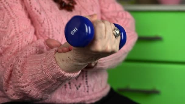 Elderly woman in pink jumper with dumbbell try the recovery of joints — Stock Video