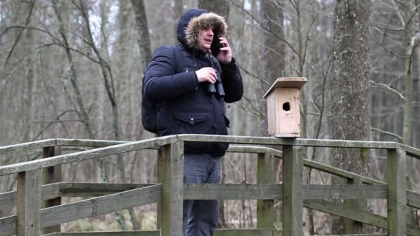 Ornitologista com binóculos e smartphone perto de gaiola de pássaro — Vídeo de Stock
