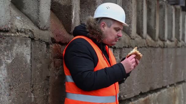 Рабочий ест гамбургер на открытом воздухе — стоковое видео