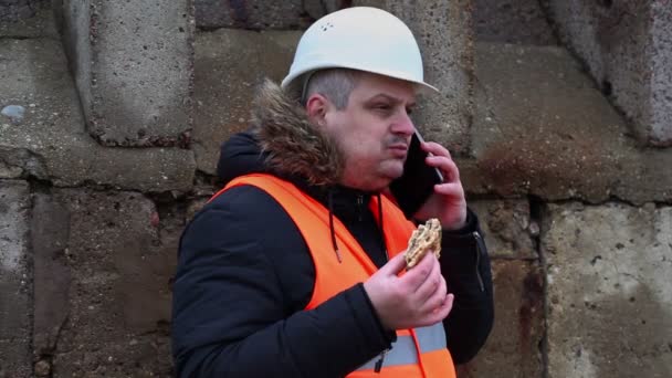 Arbeiter mit Hamburger spricht auf Smartphone im Freien — Stockvideo