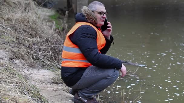 Экологический инспектор говорит на смартфоне у реки ранней весной — стоковое видео
