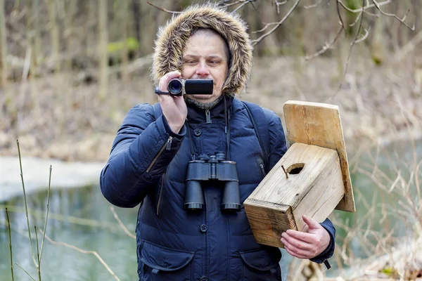 Ornithologist with camcorder and bird cage near river — Stock Photo, Image